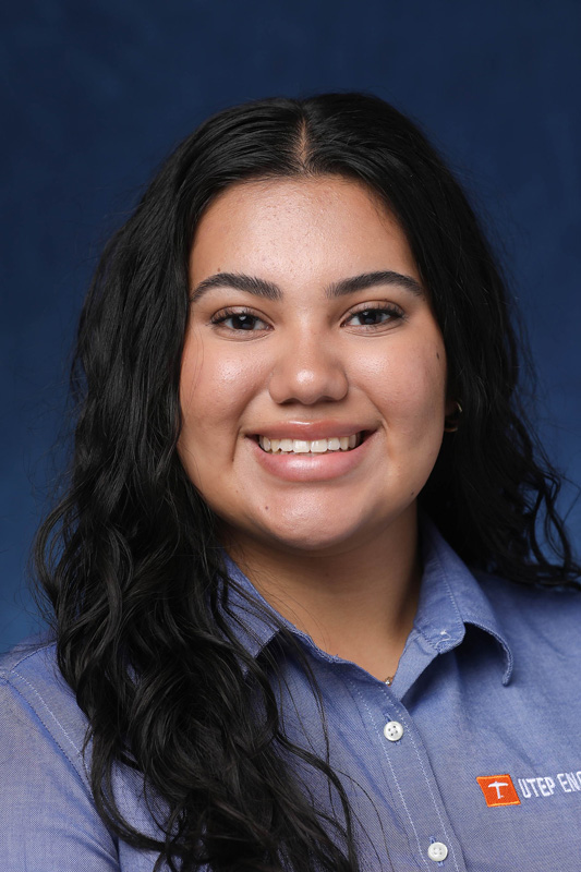 Professional headshot of Cosette Ruiz wearing a light blue button-down shirt with a UTEP logo, facing the camera against a blue studio background.